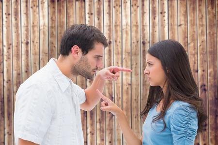 Angry couple pointing at each other against wooden planksの写真素材