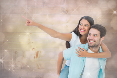 Happy casual man giving pretty girlfriend piggy back against shimmering light design on greyの写真素材