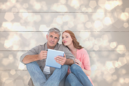Casual couple sitting using tablet against light glowing dots design patternの写真素材
