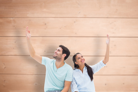 Cute couple sitting with arms raised against overhead of wooden planksの写真素材