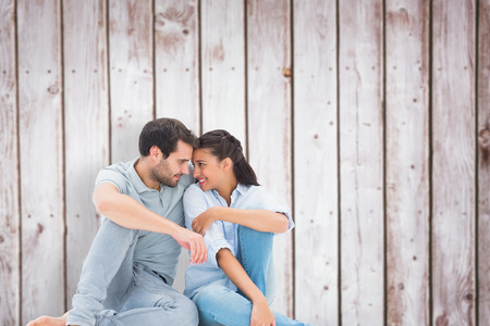 Cute couple sitting close together against wooden planksの写真素材