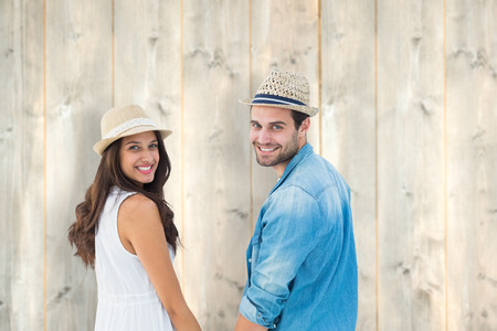 Happy hipster couple holding hands and smiling at camera against pale wooden planksの写真素材