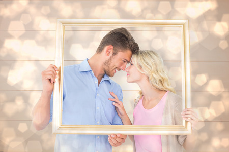Attractive young couple holding picture frame against light glowing dots design patternの写真素材