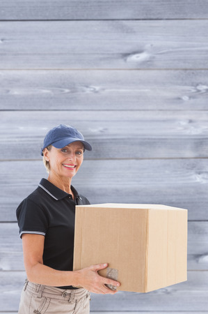 Happy delivery woman holding cardboard box against wooden planksの写真素材