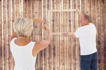 Mature couple hanging up picture frame against wooden planksの写真素材