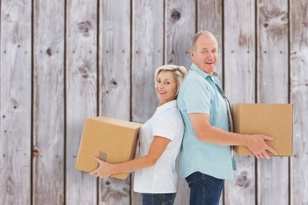 Happy older couple holding moving boxes against wooden planksの写真素材