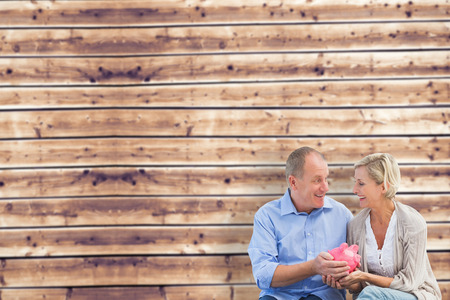 Happy mature couple holding piggy bank against wooden planks backgroundの写真素材