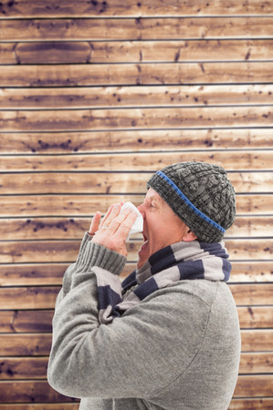 Sick mature man blowing his nose against wooden planks backgroundの写真素材
