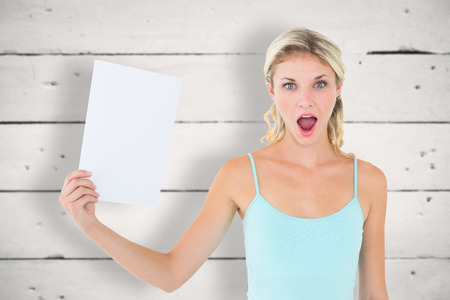 Shocked blonde holding a sheet of paper against white woodの写真素材
