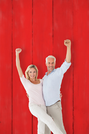 Smiling couple cheering at the camera against red wooden planksの写真素材