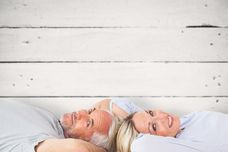 Smiling couple lying and looking at camera against white woodの写真素材