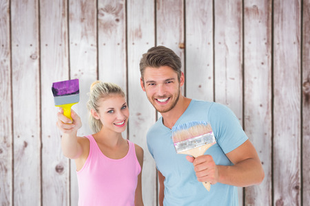 Young couple smiling and holding paintbrushes  against wooden planksの写真素材