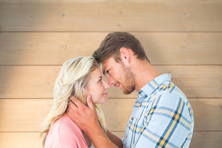Attractive couple smiling at each other against bleached wooden planks backgroundの写真素材
