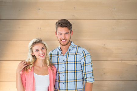 Attractive young couple smiling at camera against bleached wooden planks backgroundの写真素材