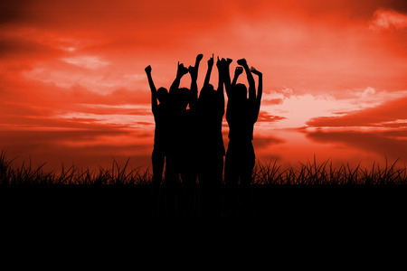 Silhouette of cheering people against red sky over grassの写真素材