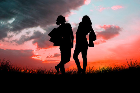 Silhouette of girls holding shopping bags against red sky over grassの写真素材
