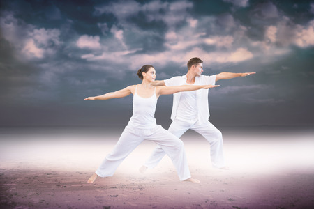 Peaceful couple in white doing yoga together in warrior position against dark cloudy skyの写真素材
