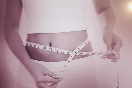 Midsection of woman measuring waist against greyの写真素材