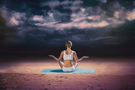 Fit woman sitting in lotus pose  against dark cloudy skyの写真素材