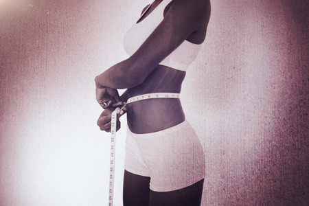 Young woman measuring her waist during diet against weathered surfaceの写真素材