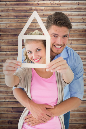 Young couple hugging and holding house outline against wooden planksの写真素材