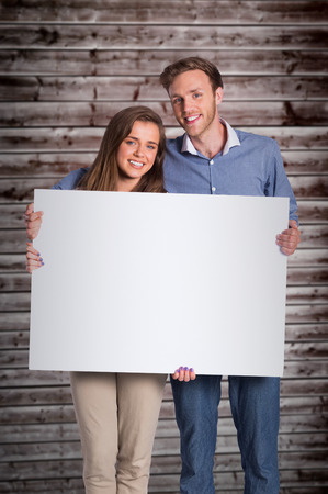 Full length portrait of couple with blank board against wooden planksの写真素材