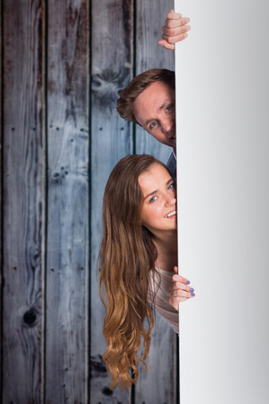 Portrait of young couple with blank board against grey wooden planksの写真素材