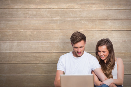Young couple using laptop on floor against wooden surface with planksの写真素材