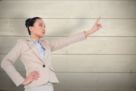 Unsmiling asian businesswoman pointing against bleached wooden planks backgroundの写真素材