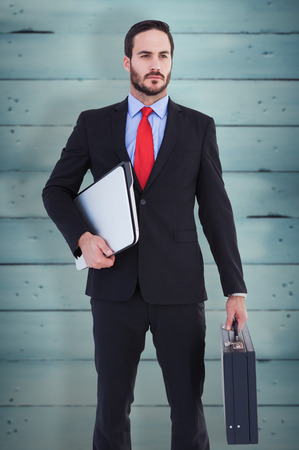 Handsome businessman holding briefcase and laptop against wooden planksの写真素材