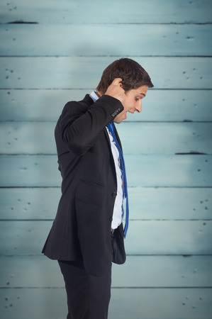Thinking businessman scratching head against wooden planksの写真素材