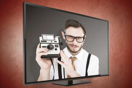 Geeky hipster holding a retro camera against orange
