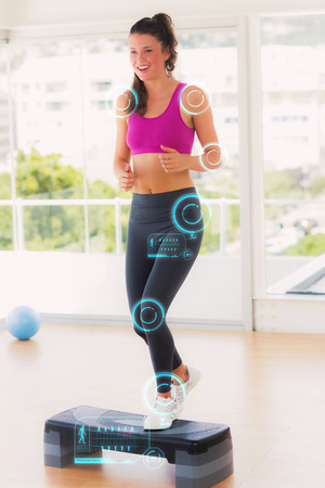 Full length of a fit woman performing step aerobics exercise against fitness interfaceの写真素材