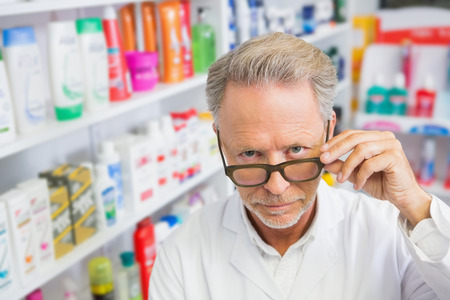Serious pharmacist holding his glasses in the pharmacyの写真素材