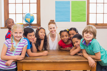 Cute pupils and teacher smiling at camera in classroom at the elementary school