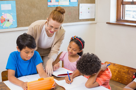 Cute pupils getting help from teacher in classroom at the elementary schoolの写真素材