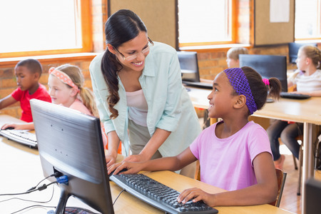 Cute pupil in computer class with teacher at the elementary schoolの写真素材