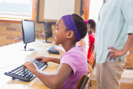 Cute pupil in computer class with teacher at the elementary schoolの写真素材