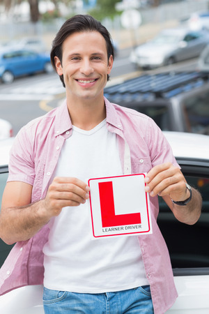 Learner driver smiling and holding l plate in front of his carの写真素材
