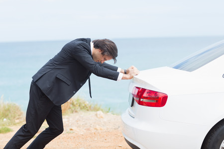 Businessman pushing his car at the side of the roadの写真素材