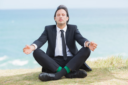 Peaceful businessman sitting in lotus pose relaxing in grassの写真素材