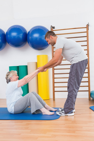 Trainer working with senior woman on exercise mat in fitness studioの写真素材