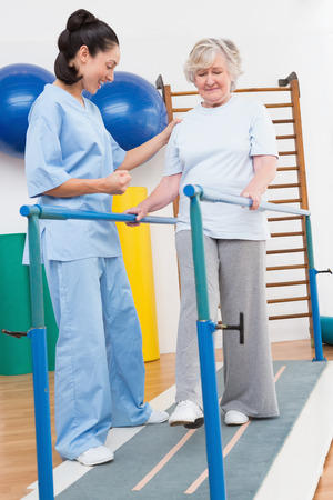 Senior woman walking with parallel bars with therapist in fitness studioの写真素材