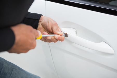 Thief breaking into car with screwdriver in broad daylight