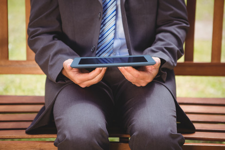 Businessman using tablet in the park on a sunny dayの写真素材