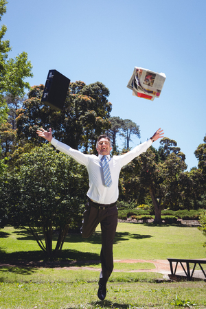 Businessman throwing briefcase and newspaper on a sunny dayの写真素材