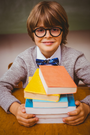 Portrait of cute little boy with stack of books in classroomの写真素材