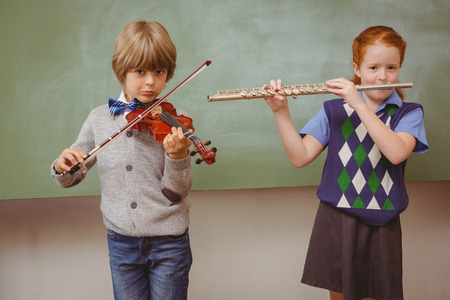 Portrait of cute little students playing flute and violin in classroomの写真素材