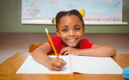 Portrait of cute little girl writing book in classroom