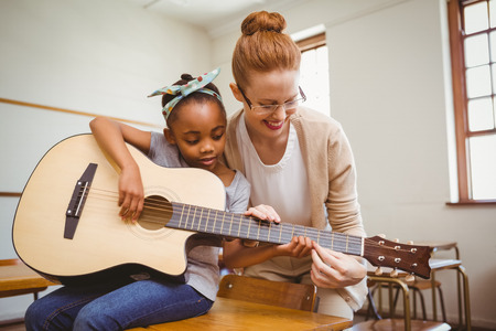 Portrait of teacher teaching cute little girl to play guitar in classroomの写真素材
